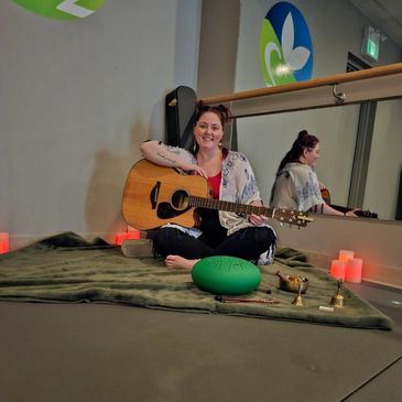 Woman sitting cross-legged with a guitar and candles.