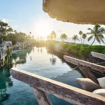 Sunset view over a serene tropical lagoon with palm trees and a cozy hammock seating area.