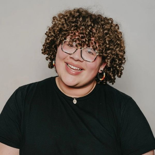 Smiling person with curly hair and glasses.