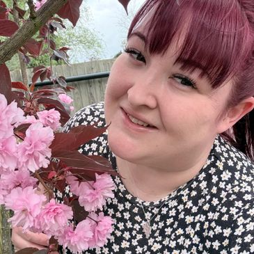 Smiling woman with red hair admiring pink blossoms outdoors.