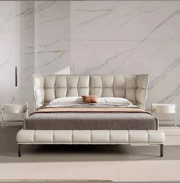 Modern bedroom with a tufted white leather bed and marble wall.