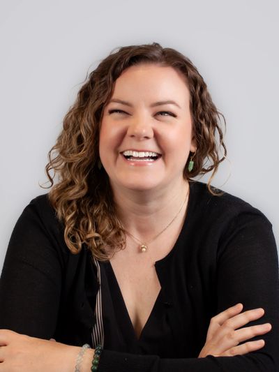 Woman with curly hair laughing joyfully against a gray background.