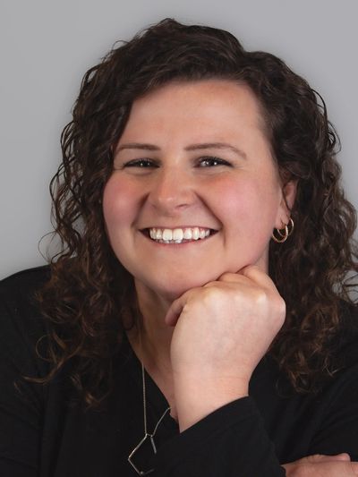Smiling woman with curly hair resting chin on hand against gray background.
