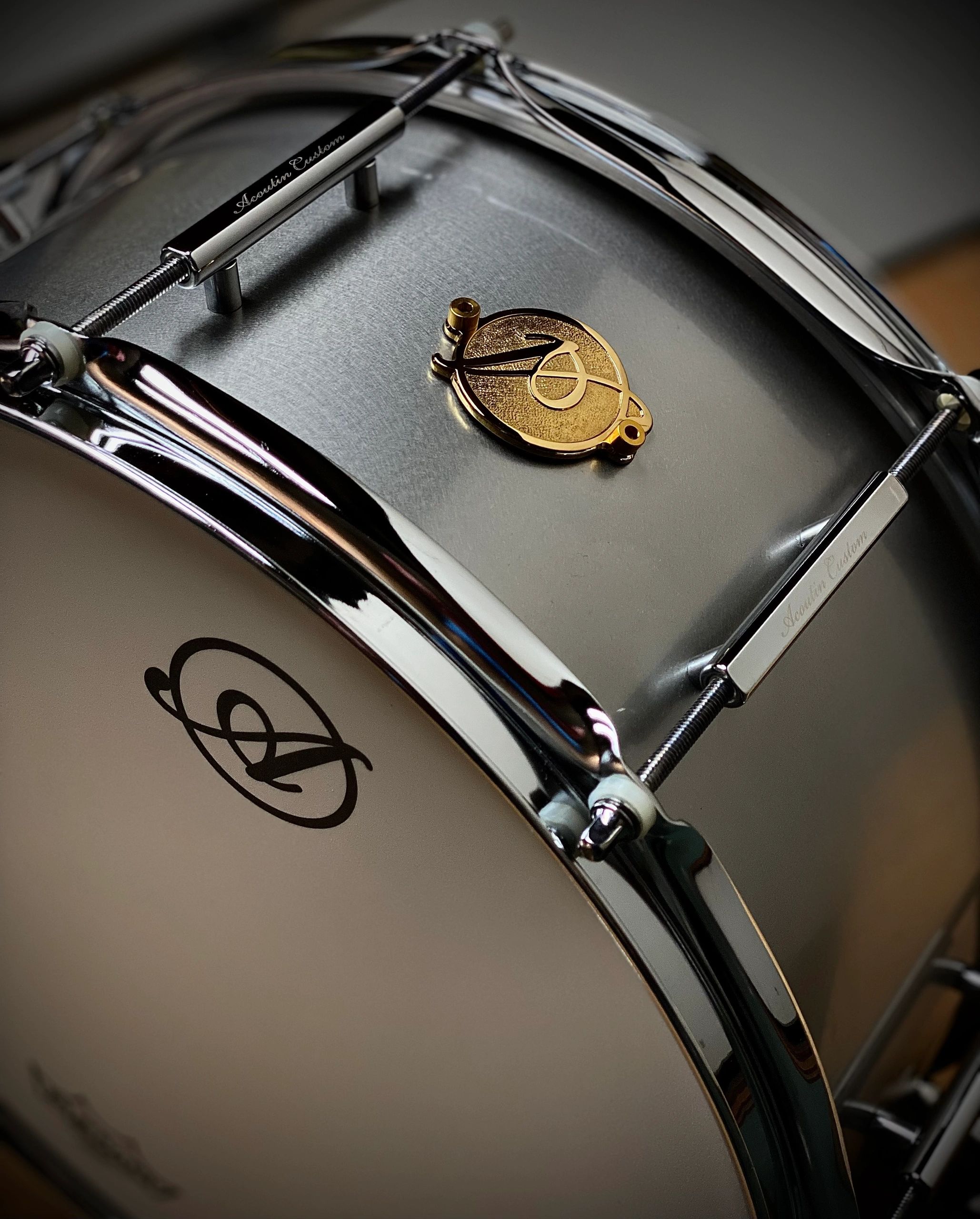 Close-up of a polished snare drum with a unique emblem and tuning rods.