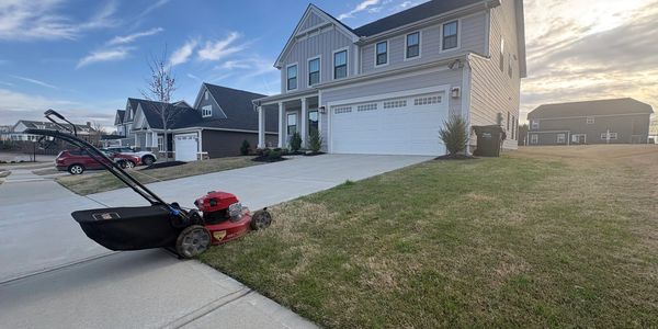 Lawn mower parked on a driveway beside a house on a sunny day.