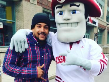 Man posing with a large mascot in a white and red costume on a city street.