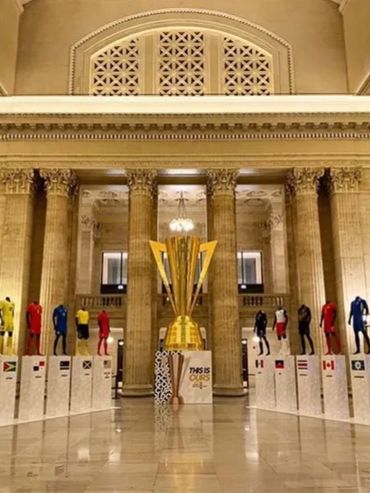 Large trophy display surrounded by mannequins in various national soccer jerseys.