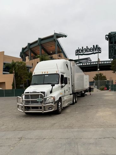 White semi-truck parked near a stadium with cloudy sky.