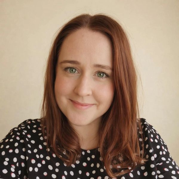 Smiling woman with red hair wearing a black polka dot top.