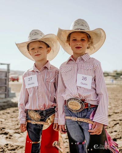 Two children dressed as cowboys with hats and belts.