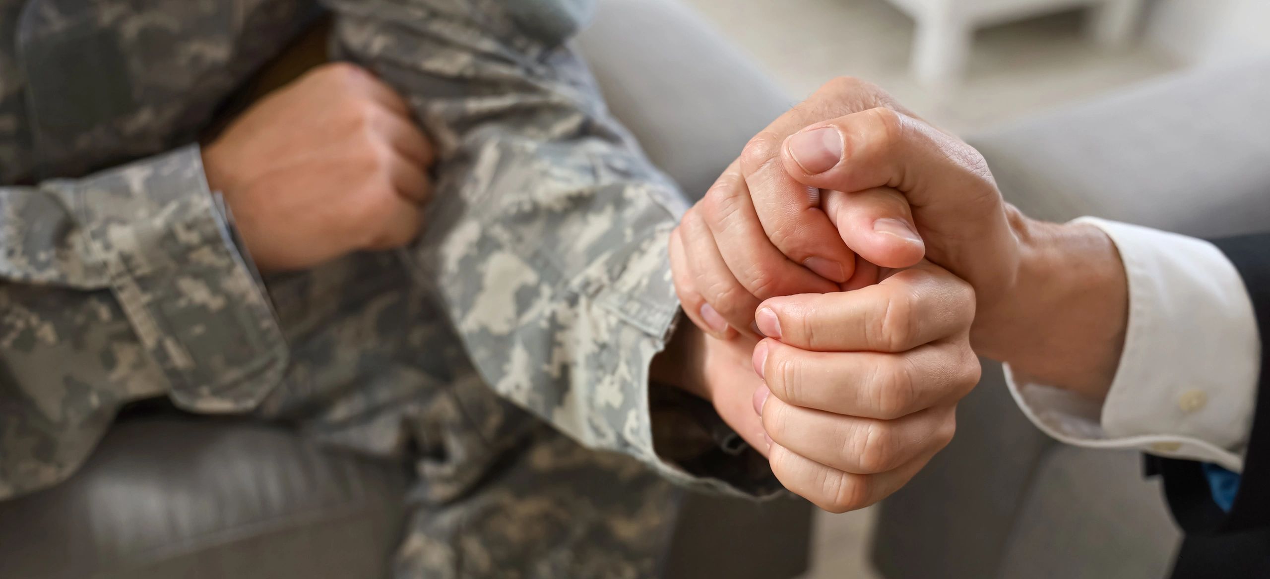 Close-up of a military member's hand being held by a civilian in a suit.