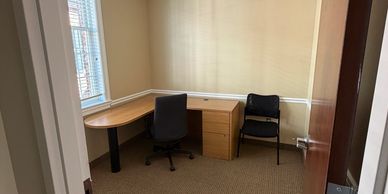 Small office with a wooden desk and two chairs near a window.