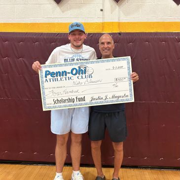 Two men holding a large scholarship check indoors.