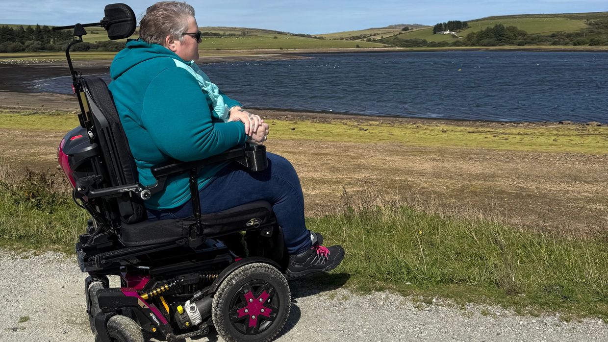 Jayne sat in her powerchair enjoying an accessible lakeside trail, in views of hills and water