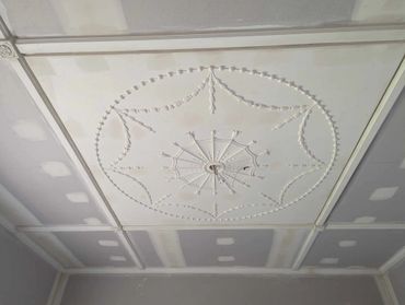 Ceiling with ornate plasterwork and unfinished drywall patches.