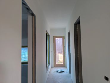 Narrow hallway under renovation with a glass door and painting supplies on the floor.