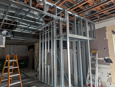 Construction site with metal framing and ladders indoors.