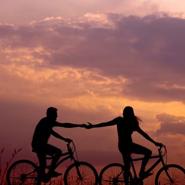 Two silhouettes of bikers. One biker is reaching back to the other biker to show a helping hand. 