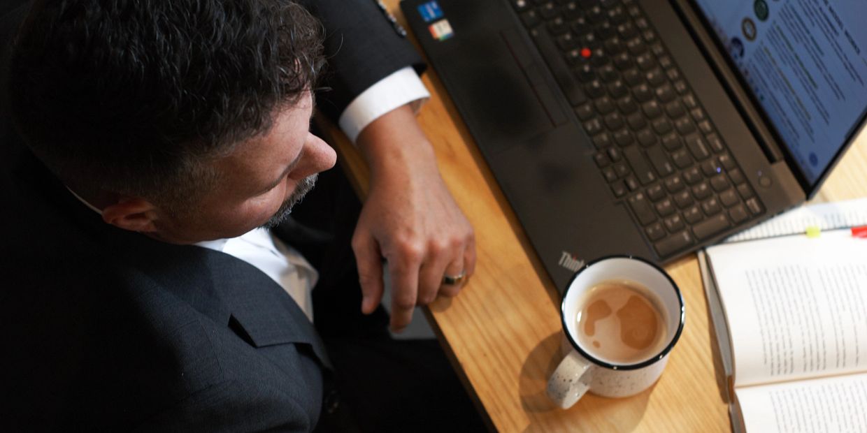 Man in a suit working with laptop, coffee, and documents.