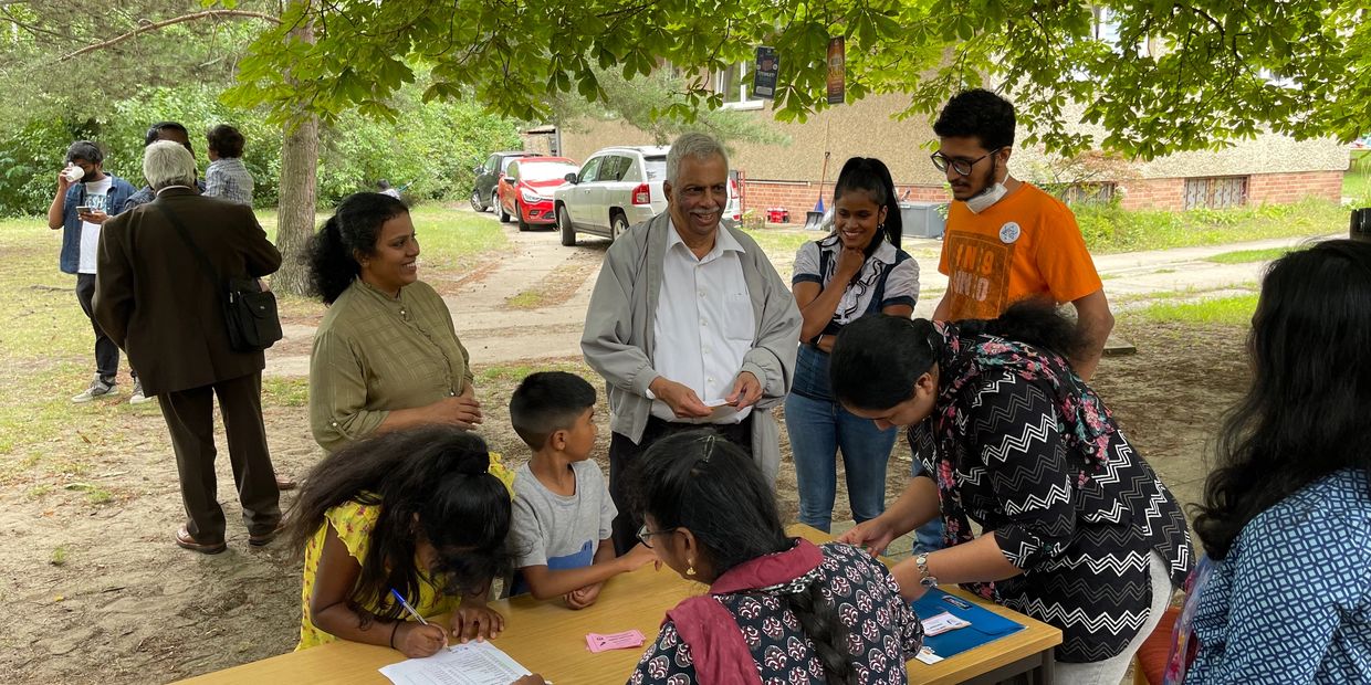 People socializing and registering at an outdoor event under a tree.