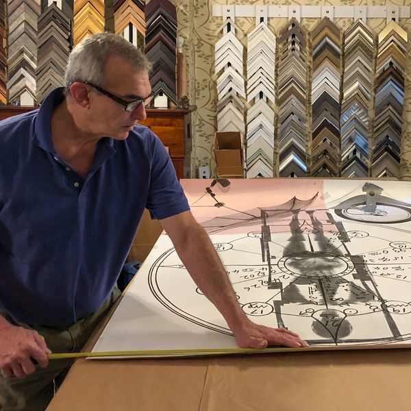 Master custom framer measuring oversize print during consultation in showroom frame samples