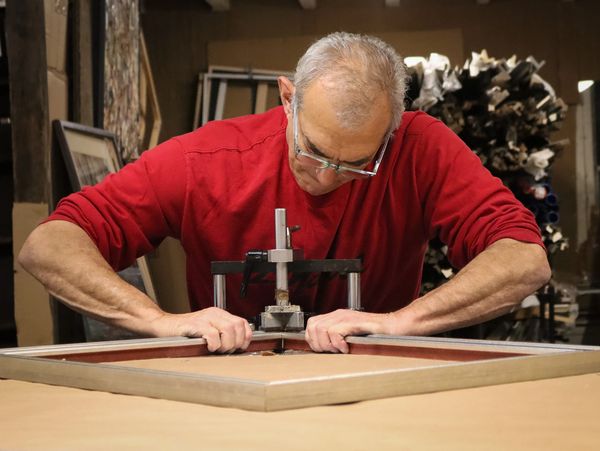 Master custom framer joining silver and blue frame in home workshop