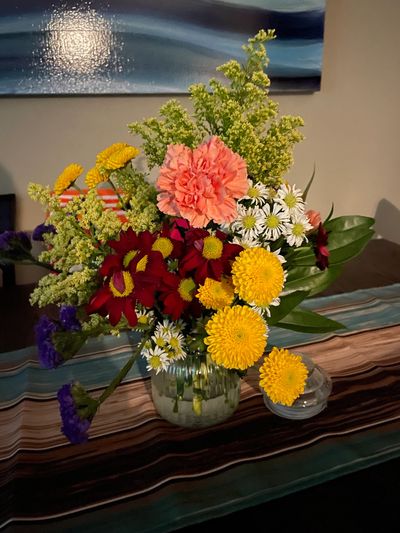 Colorful mixed flower bouquet in a glass vase on a striped table runner.