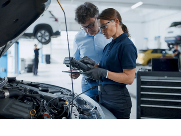 Female mechanic using diagnostic tool while consulting with a man in a car repair shop.