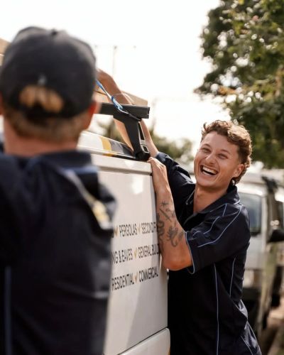 Two men loading items into a vehicle, one smiling.