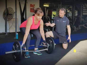 Woman lifting barbell with trainer guidance.
