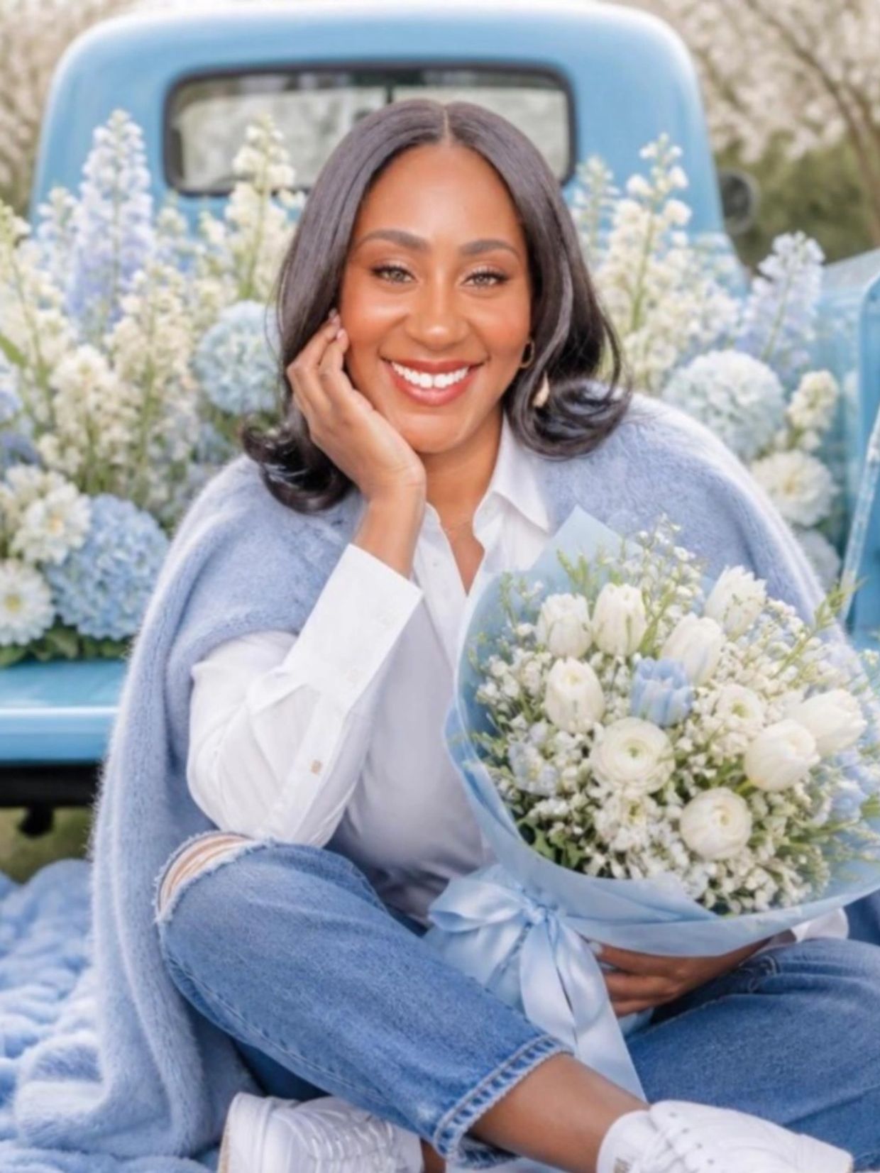 Smiling woman in jeans holding a bouquet of white and blue flowers.