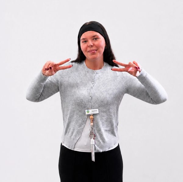 A woman in a gray cardigan shows peace signs with both hands.