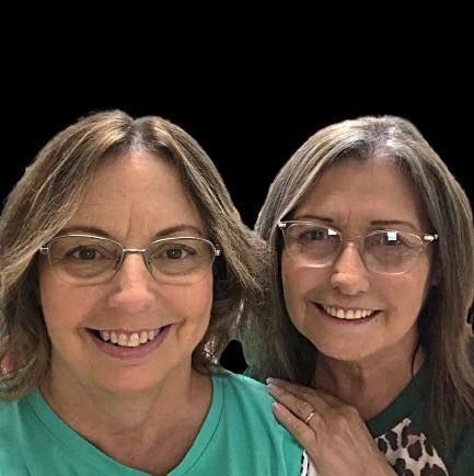 Two smiling women wearing glasses posing together against a black background.