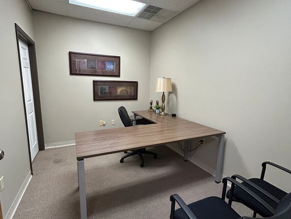 Simple office with L-shaped desk and three chairs.