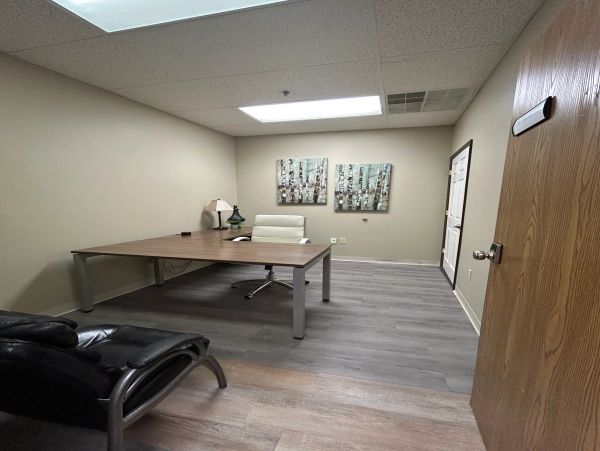 A simple office with a desk, chair, and wall art.