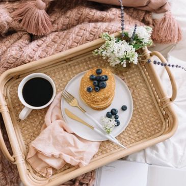 Breakfast tray with pancakes, coffee, and flowers on cozy bedding.