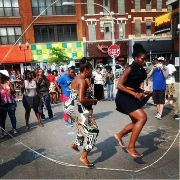 Two women dancing barefoot in the street during a lively outdoor event.