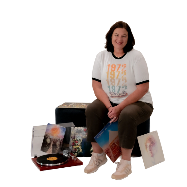 Woman smiling while sitting near a record player and vinyl records.