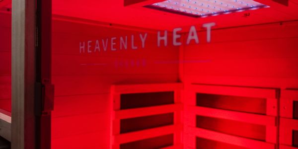 Interior of a red-lit sauna with 'Heavenly Heat' text on the glass door.