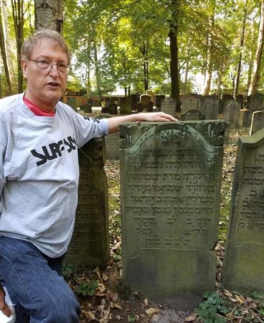 Image of a persMan kneeling beside weathered Hebrew gravestone outdoorson