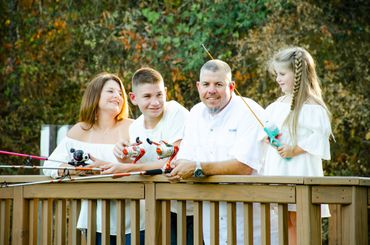 A family of four fishing together on a wooden deck in nature.