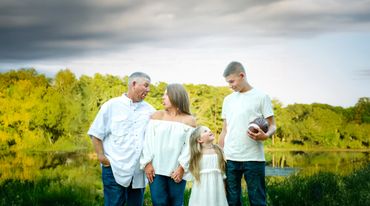 Family making funny faces outdoors near a lake with trees in the background.