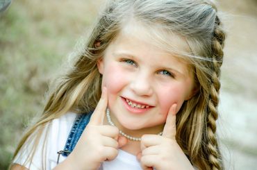 Smiling young girl with braided hair and pearl necklace outdoors.