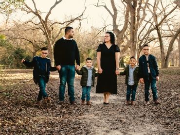 A family of six holding hands in a wooded park during autumn.