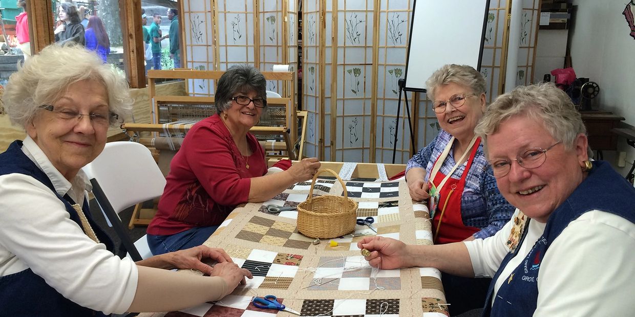 Grand Lake Quilt Guild members teaching quilt tying during Pioneer Day at Har-Ber Village. 
