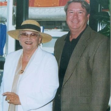 A man smiling with a woman wearing a white jacket and a hat with a black ribbon