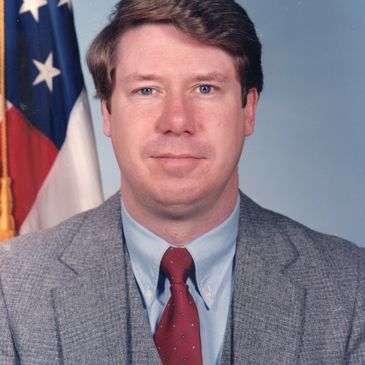 A man with a neutral facial expression, wearing a professional outfit