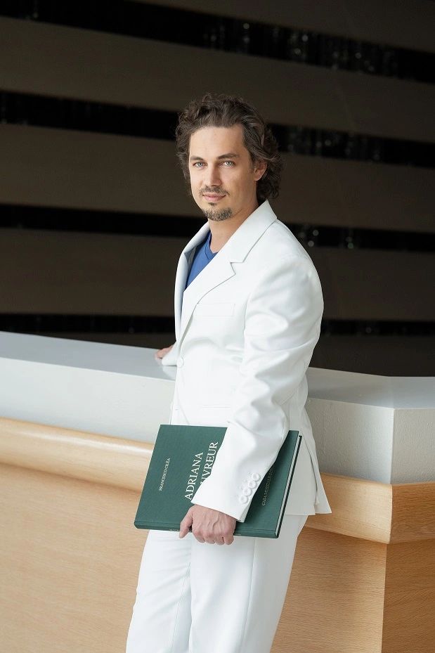 Man in white suit holding a green book, posing confidently.