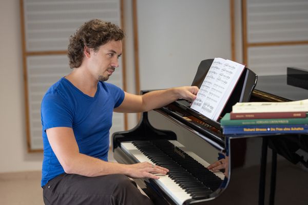 Man in blue shirt adjusting sheet music on a grand piano.