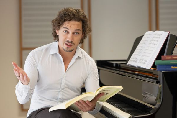 Man explaining music theory with book at piano.